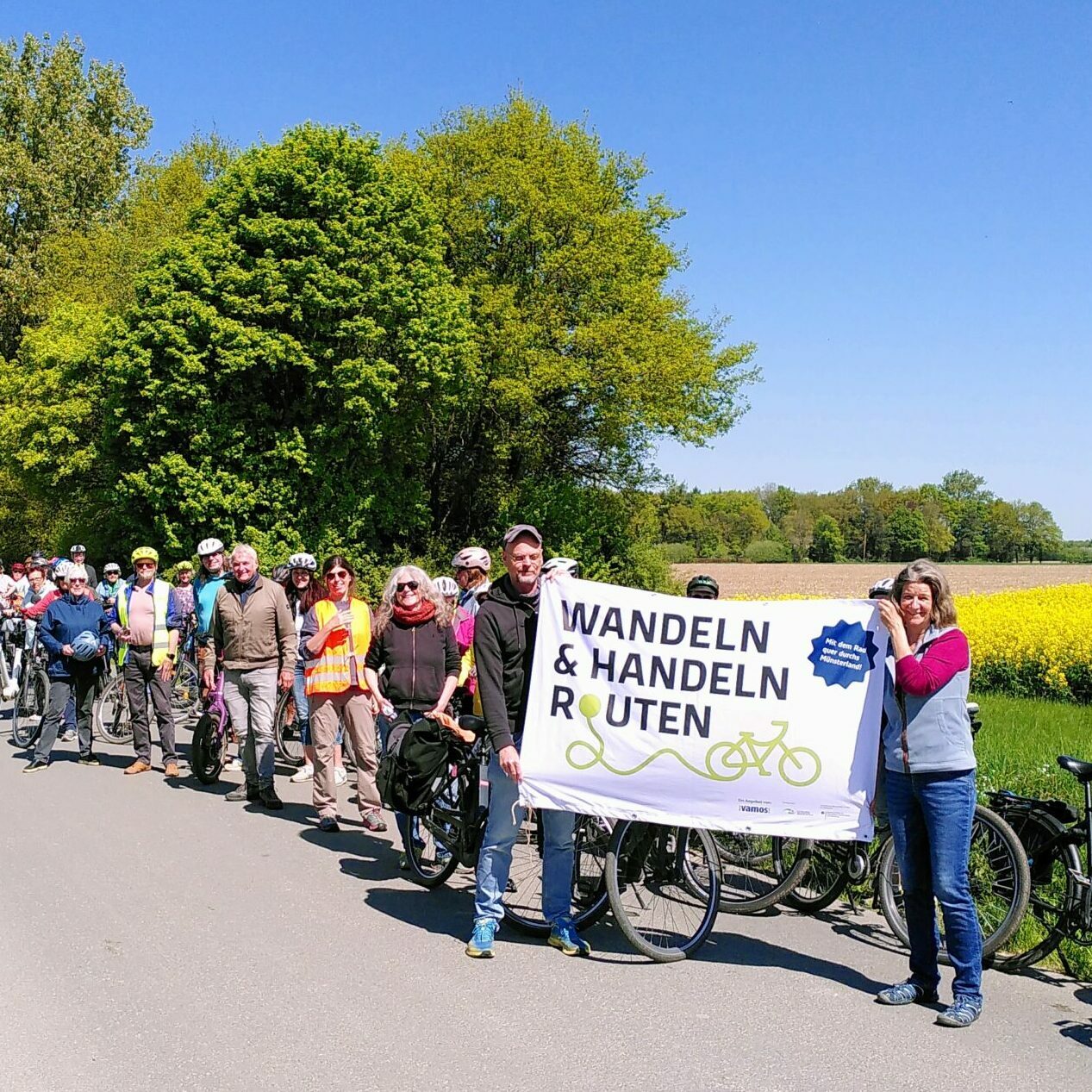 Gruppe mit Plakat in Hand vor Rapsfeld